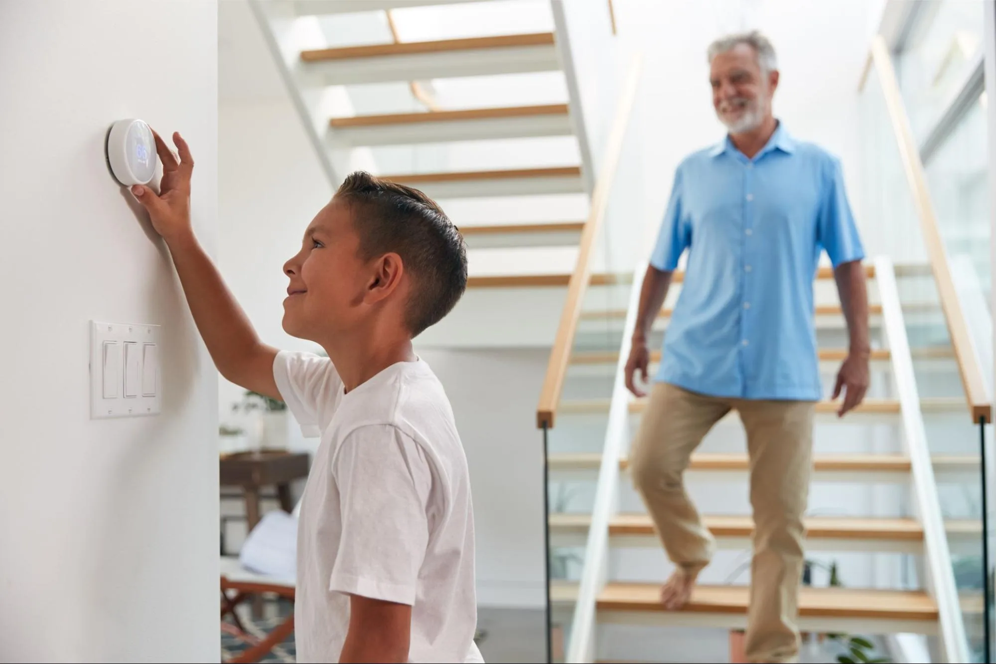A child adjusts the thermostat with their father in the background. 